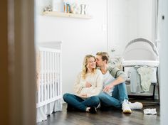 a man and woman sitting on the floor next to a baby crib