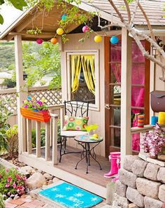 an outdoor patio with a table and chairs on the porch, surrounded by flowers and trees