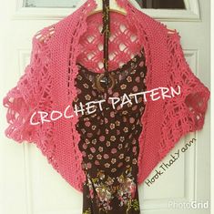 a pink crocheted shawl hanging on a door with a brown dress underneath it