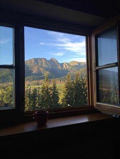 a window with mountains in the background and a cup sitting on a table next to it