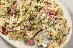 a plate full of pasta salad with peas and tomatoes on it, ready to be eaten