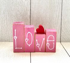 a wooden block with the word love written on it and a red heart placed between two blocks