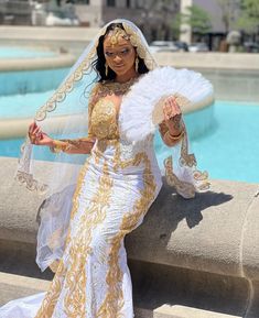 a woman in a white and gold wedding dress holding a fan next to a pool