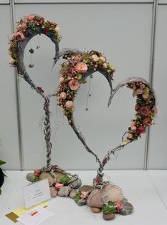 two hearts made out of branches with flowers and leaves on the table next to it