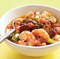 a white bowl filled with shrimp and beans next to a yellow napkin on top of a table