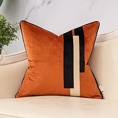 an orange and black pillow sitting on top of a white couch next to a potted plant