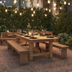 an outdoor dining area with lights strung over the table and benches in front of it