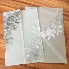 three envelopes with floral designs on them sitting on a wooden table next to each other