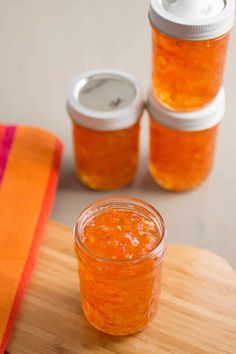 three jars filled with orange colored liquid sitting on top of a wooden cutting board next to an orange towel