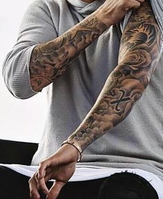 a man with tattoos on his arm sitting down and holding his hand near his face