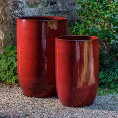 two red vases sitting next to each other in front of a stone wall and shrubbery