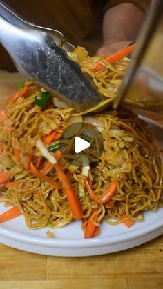 someone is cutting up some noodles on a white plate with carrots and green peppers