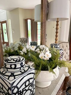 two vases with flowers in them sitting on a table next to a mirror and lamp