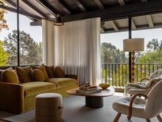 a living room filled with furniture next to a large glass window covered in white drapes