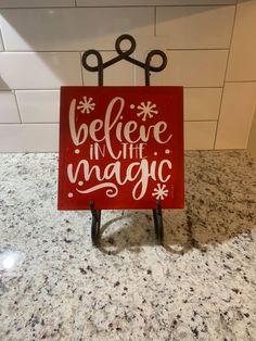 a red sign that says believe in the magic on top of a black stand with scissors