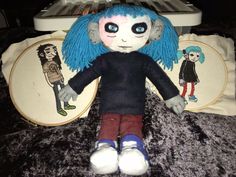 a stuffed animal with blue hair sitting next to pillows