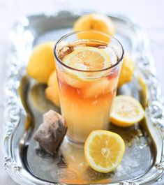 a glass filled with liquid next to sliced lemons on a silver platter,