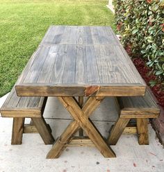 a wooden picnic table with two benches next to it on the sidewalk in front of some bushes