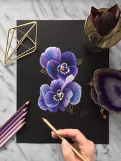 a person is drawing flowers on a piece of paper with colored pencils next to it