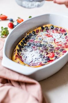 a dish with fruit and powdered sugar in it sitting on a table next to strawberries