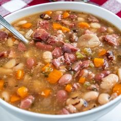 a white bowl filled with beans, ham and carrots on top of a checkered table cloth