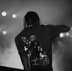 a man standing on top of a stage with his arms out in the air and lights behind him