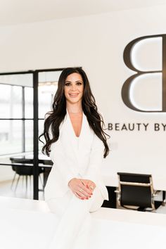 a woman sitting on top of a counter in front of a beauty by design sign