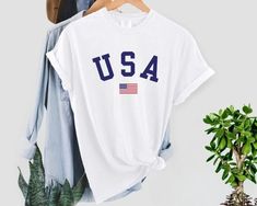 This classic USA Flag t-shirt is perfect for celebrating the 4th of July with friends and family, or for supporting the home team when they compete this summer in Paris. These soft-washed Comfort Colors garment-dyed t-shirts are 100% cotton, bringing extra coziness to your wardrobe, while the relaxed fit makes it an excellent daily choice. The unisex cut is true to size but if you want an oversized look, order one or two sizes up.  The double-needle stitching throughout the tee makes it highly d Team Tshirt, Usa Christmas, Independence Day Gift, Paris Summer, Usa Tee, Comfort Colors Tshirt, Home Team, Flag Shirt, Flag Tshirt