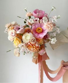 a bouquet of flowers is being held by someone's hand with a pink ribbon