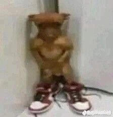 a teddy bear standing up against a wall with shoes on the floor next to it