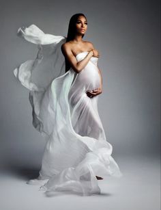 a pregnant woman wearing a white dress and holding her belly in the air while standing on a gray background