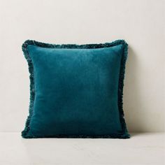 a teal pillow with fringe trim on the front and back of it, against a white wall