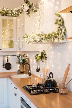 a kitchen decorated for christmas with lights and greenery on the counter top, along with cooking utensils