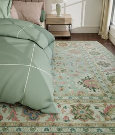 a bed with green sheets and pillows in a room next to a large rug on the floor