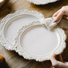 two people are holding plates with white trimmings on them and one person is cleaning the plate