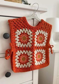 an orange crocheted bag hanging from a hook on a white cabinet in a room