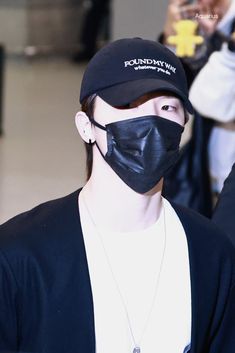 a man wearing a black mask and jacket at an airport with people in the background