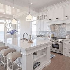 a large kitchen with white cabinets and an island in the middle of the room that has four stools on it