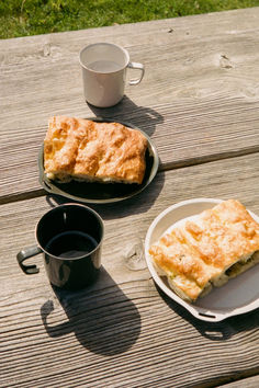 two plates with pastries on them sitting on a picnic table next to cups and saucers