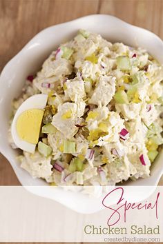 a white bowl filled with chicken salad on top of a wooden table next to an egg