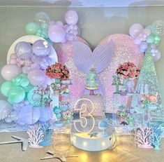 a table topped with balloons and cake next to a wall covered in mermaid themed decorations