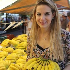 a woman holding a bunch of bananas in front of a table full of other bananas