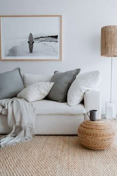 a living room with a white couch and some pillows on the floor next to a lamp