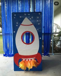 a cardboard rocket ship sitting on top of a cement floor in front of blue curtains