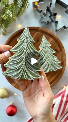 someone is holding a small christmas tree cookie in front of a plate with ornaments on it