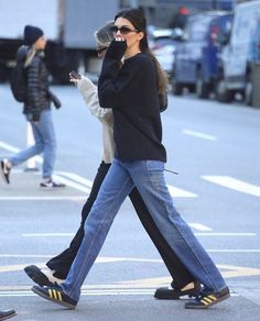 a woman walking down the street while talking on her cell phone with another person in the background