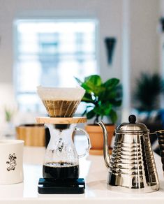 a coffee pot sitting on top of a counter next to two cups