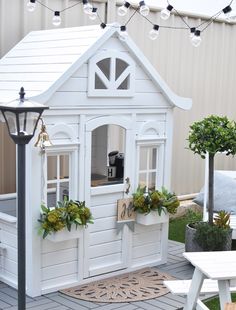 a small white doll house with windows and doors on the outside, surrounded by greenery