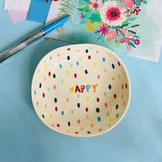 a bowl with the words happy written on it next to a pen and paper flowers