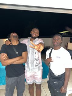 three men standing next to each other in front of a swimming pool with one pointing at the camera